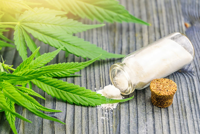 Marijuana leaves and a bottle of CBD powder on a wooden surface